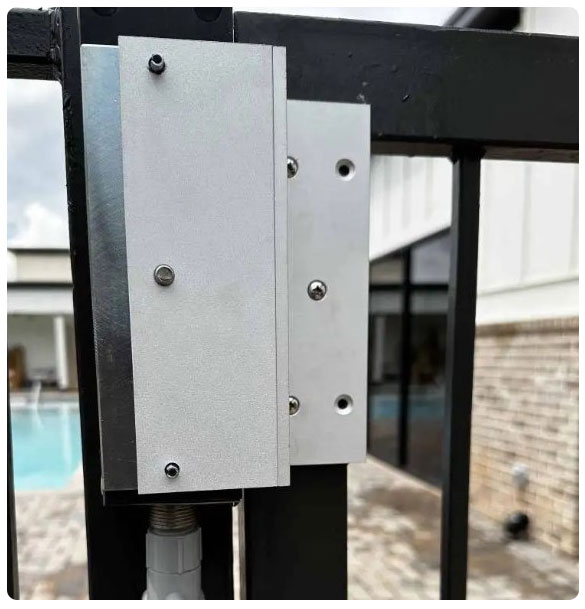 Gate operator system installation, featuring a secure electronic lock mechanism on a black metal gate, with a pool and building in the background, emphasizing access control solutions for property security.