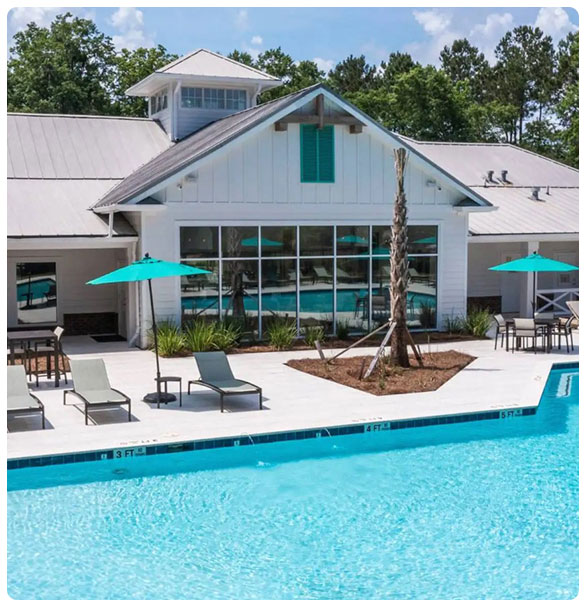 Clubhouse and pool area at Canvas at Savannah, featuring lounge chairs, umbrellas, and modern architecture, enhancing resident amenities and community experience.