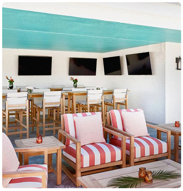 Outdoor seating area at Hotel Simone featuring striped lounge chairs, wooden tables, and multiple mounted televisions for guest entertainment, enhancing the dining experience and operational efficiency.