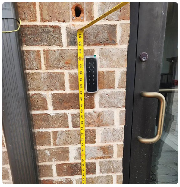 Access control system installation with keypad and measuring tape against brick wall, highlighting security features for enhanced building safety.