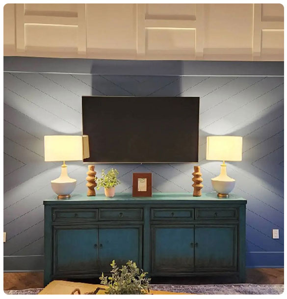 Modern living room setup featuring a wall-mounted TV, decorative lamps, a wooden console table, and a potted plant, illustrating audio and visual installation solutions by SAV Systems.