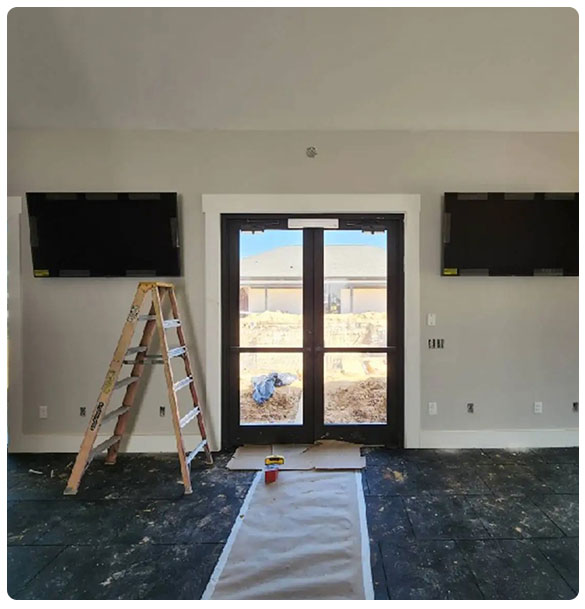 Interior view of a room with two mounted TVs, a ladder, and a doorway leading outside, showcasing the setup for an audio-visual installation at Pointe Grand Apartments.