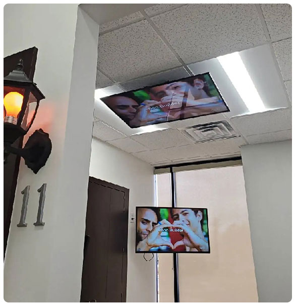 Two mounted TVs displaying content in a dental treatment room, featuring a ceiling-mounted screen and a wall-mounted screen, enhancing patient entertainment and information access at McDonough Dental Studio.
