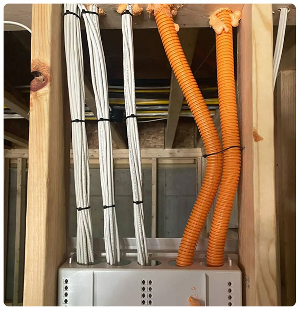 Wiring and networking infrastructure installation in a new residential construction, featuring bundled white cables and orange conduit, supporting advanced technology systems.