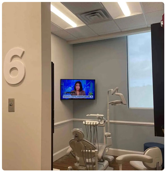 Dental treatment room featuring a TV displaying news for patient entertainment, dental chair and equipment, room number 6, modern design.