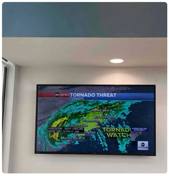 TV displaying a weather alert for tornado threat, featuring a map of affected areas, including Myrtle Beach and Fayetteville, in a dental treatment room setting.