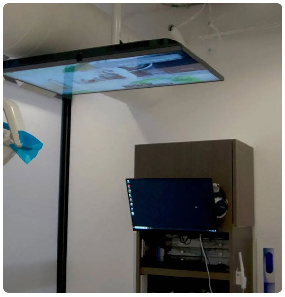 Ceiling-mounted display screen and wall-mounted computer monitor in a dental office setup, showcasing advanced AV integration for patient entertainment and information access.