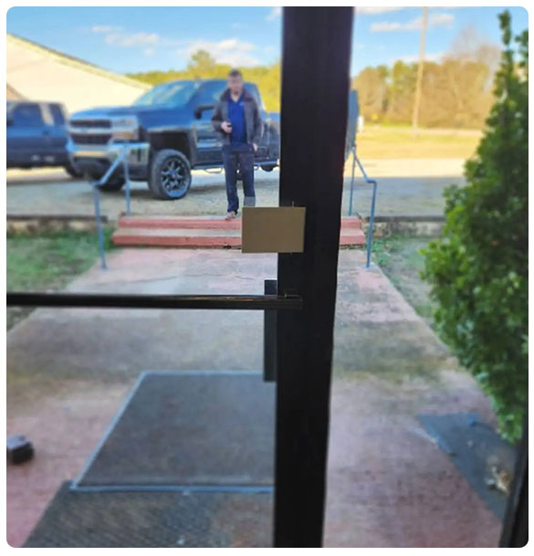 View from inside a commercial building entrance, showing a man standing outside near a black truck, with visible steps and railing leading to the entrance, reflecting the accessibility features of the newly constructed motorsport workshop by SAV Systems.