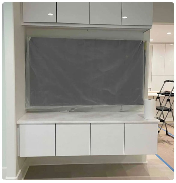 Modern white cabinetry with a concealed 75" TV installation, featuring protective covering, in a residential basement remodel by SAV Systems.