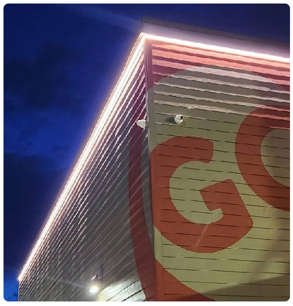 Commercial building exterior with security camera, illuminated signage, and night sky backdrop, highlighting SAV Systems' surveillance solutions.