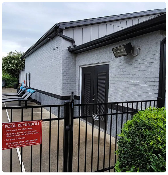 Leasing office exterior with black double doors, surrounded by a gated pool area featuring lounge chairs and a red sign detailing pool rules at Retreat at Waterside, Greenville, SC.