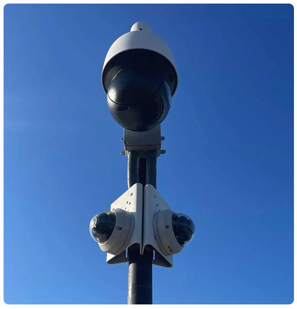 Security camera system installation with multiple camera types, mounted on a pole against a clear blue sky, enhancing safety for commercial spaces.